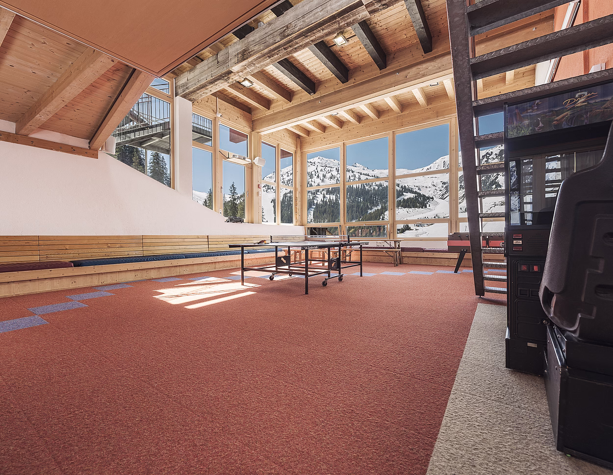 Game room with ping pong table, arcade machine, and large windows showing snowy mountains.
