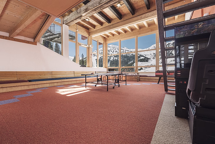 Game room with ping pong table, arcade machine, and large windows showing snowy mountains.