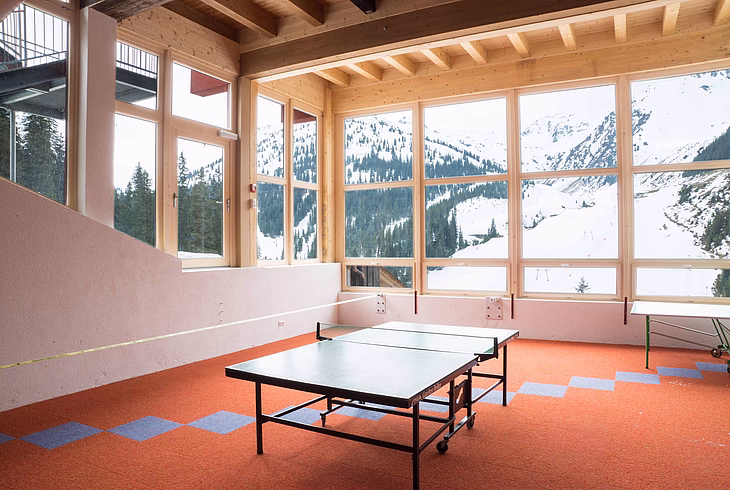 Ping pong table in a room with large windows showing snowy mountains.