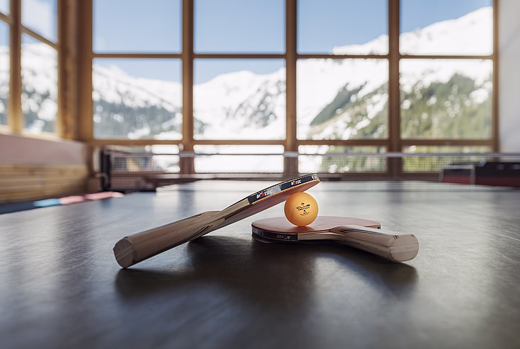 Ping pong table and bats with a snowy mountain view outside the window.