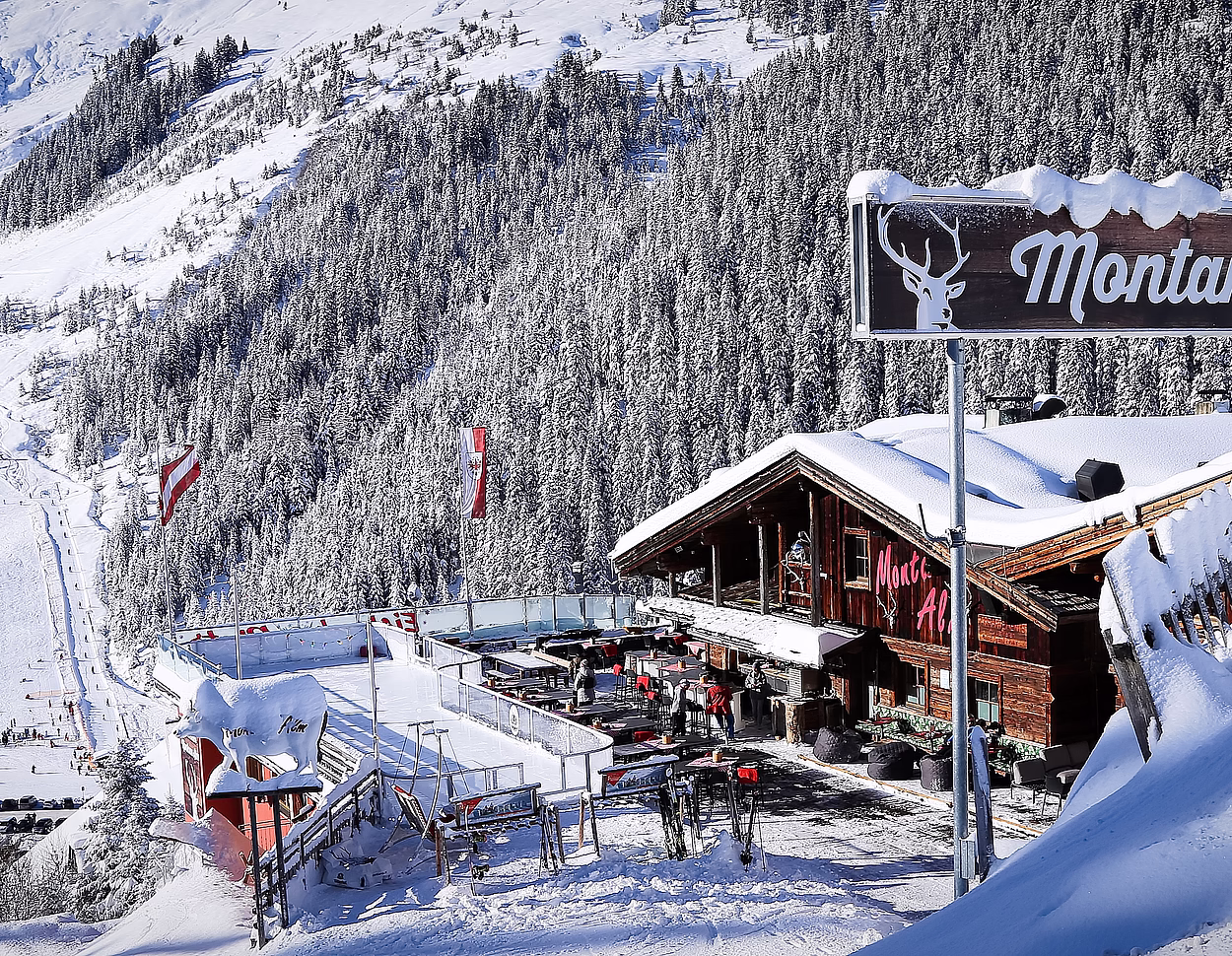 Verschneite Montana Alm Skihütte mit großem Holzschild im Vordergrund und Skipisten im Hintergrund.