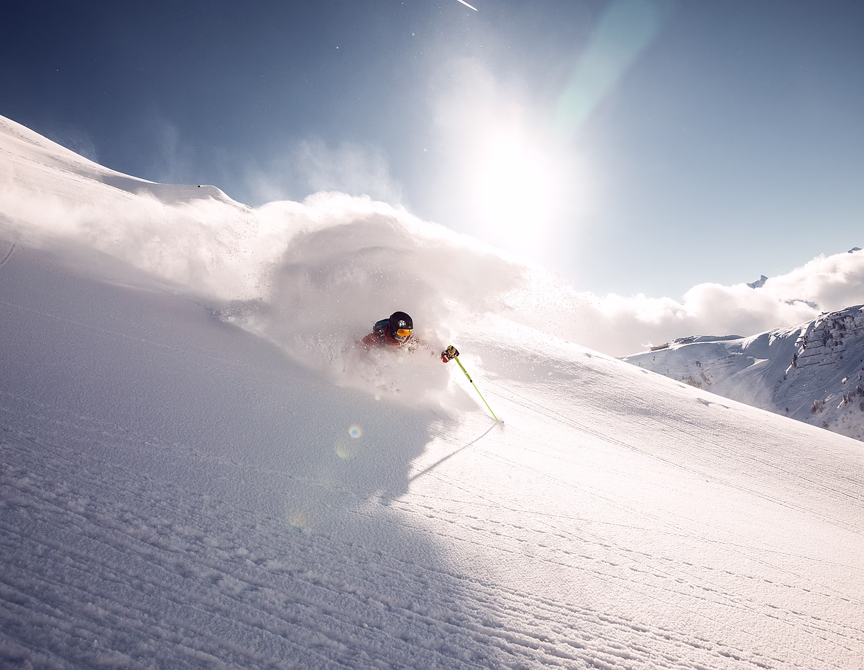 Skifahrer in einer Pulverschneewolke an einem sonnigen Hang.